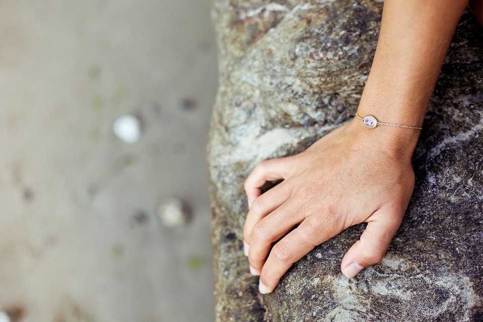 Main portant un bracelet des bijoux Arméria sur une plage bretonne