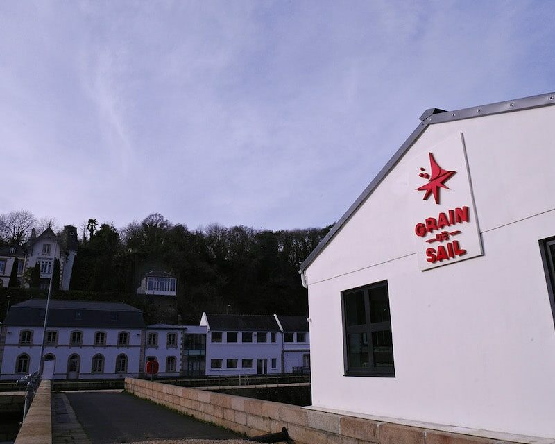 Entrepot chocolat et cafe Grain de Sail avec des bâtiments du port en fond et une forêt.