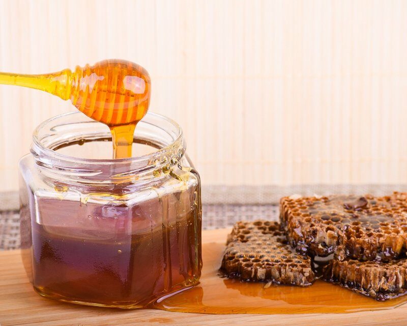 Un pot de miel avec sa cuillère et un cadran, un des ingrédients de base du chouchen