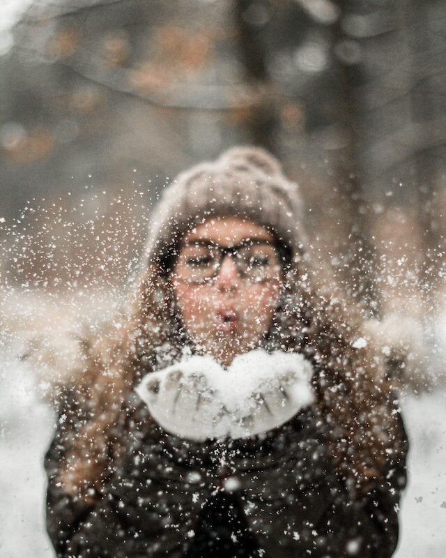 Femme qui souffle sur la neige dans ses mains